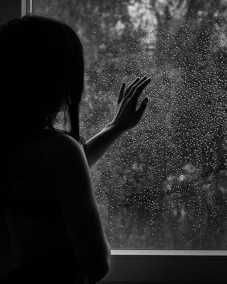 a woman standing in front of a window with rain drops on the glass and her hands up