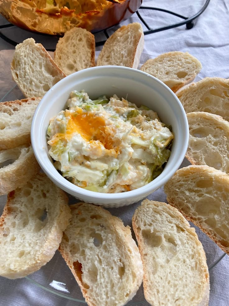 there is a bowl of food on the table with bread slices around it and an orange in the background