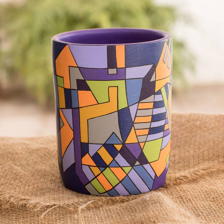 a colorful cup sitting on top of a burlly cloth covered table next to a potted plant