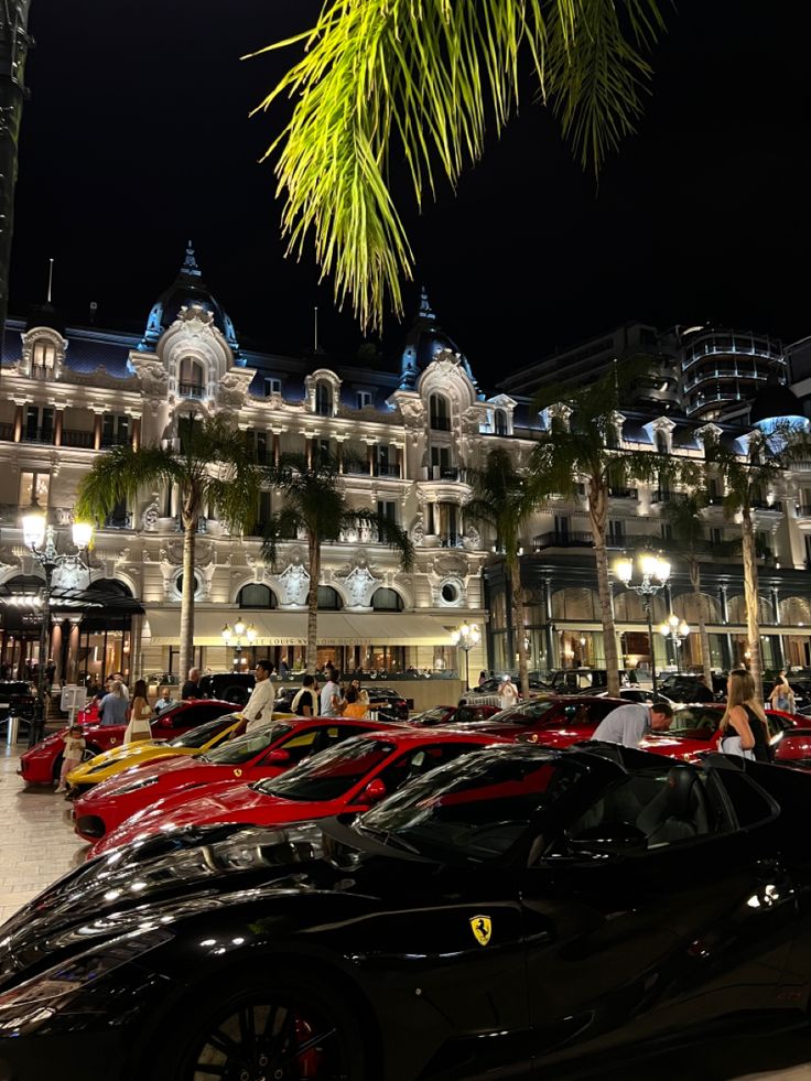 a bunch of cars are parked in front of a building at night with palm trees