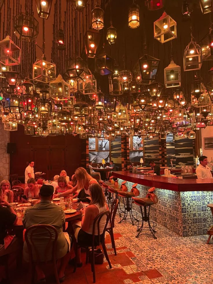 people sitting at tables in a restaurant with many lights hanging from the ceiling above them