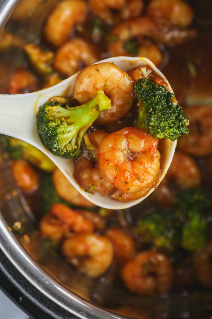 a spoon full of shrimp and broccoli in a crock pot