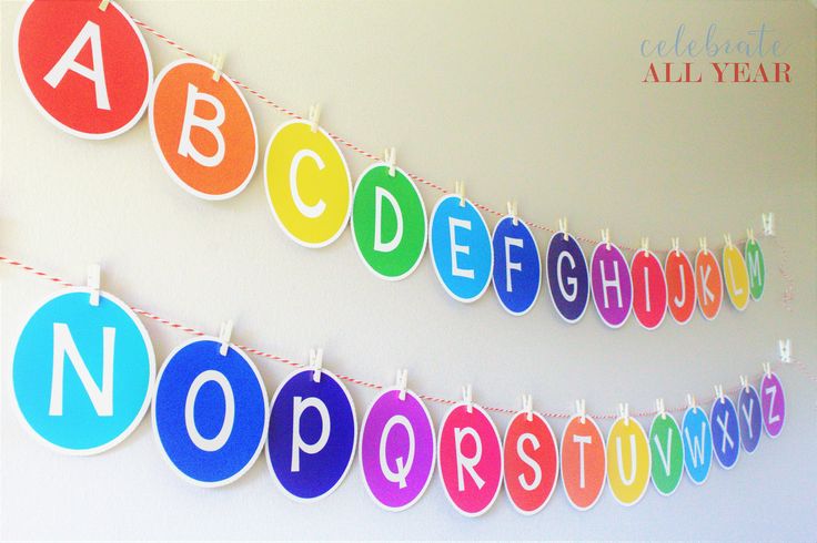 colorful paper letters and numbers hanging from clothes pins on a line in front of a white wall