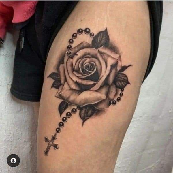 a black and white rose with rosary on the side of a woman's thigh