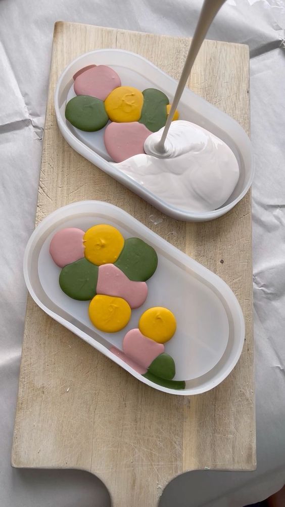 two white trays filled with colorful cookies on top of a wooden table next to each other