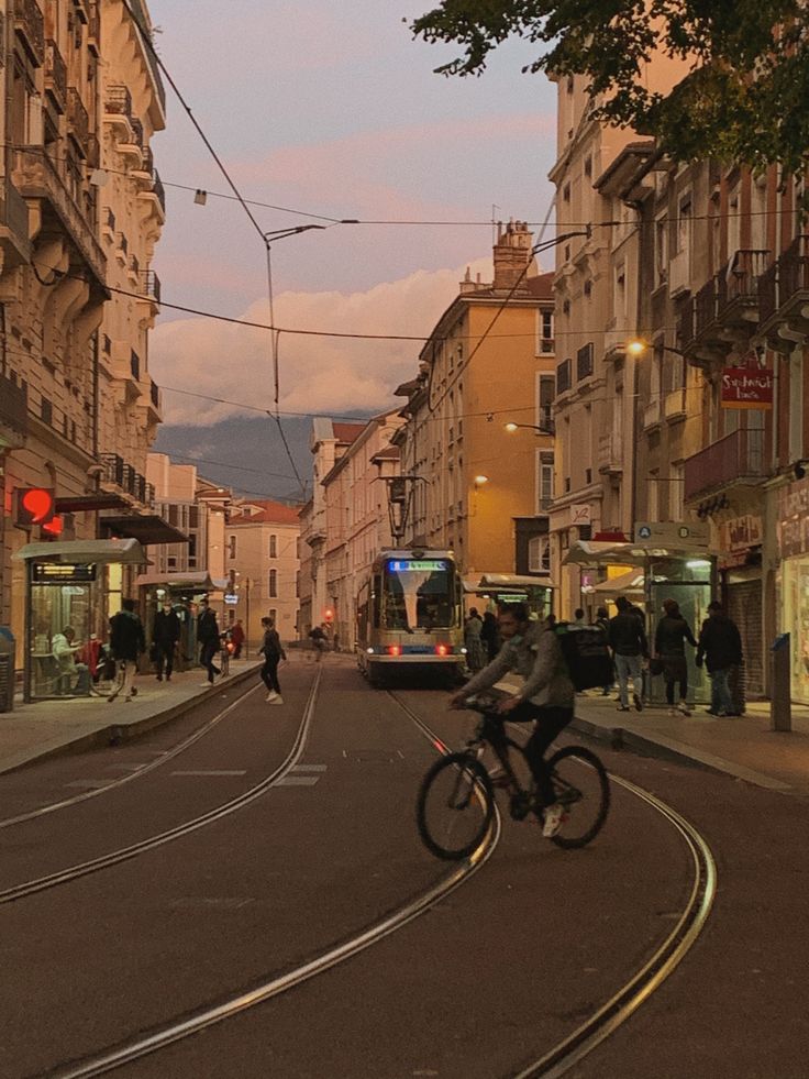 a man riding a bike down a street next to tall buildings and people walking on the sidewalk