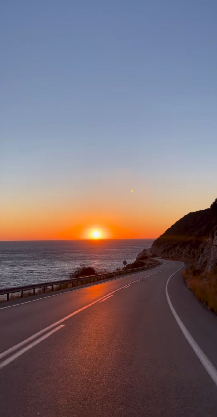 the sun is setting over the ocean and road