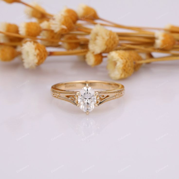 a diamond ring sitting next to dried flowers