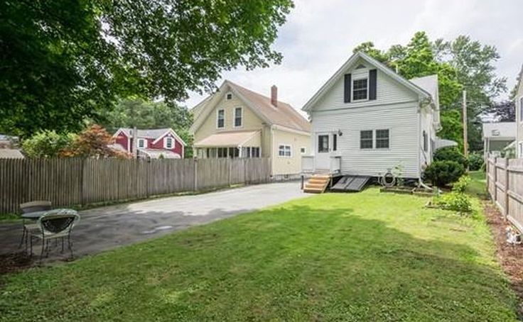 the back yard is fenced off and has grass on it, as well as two houses