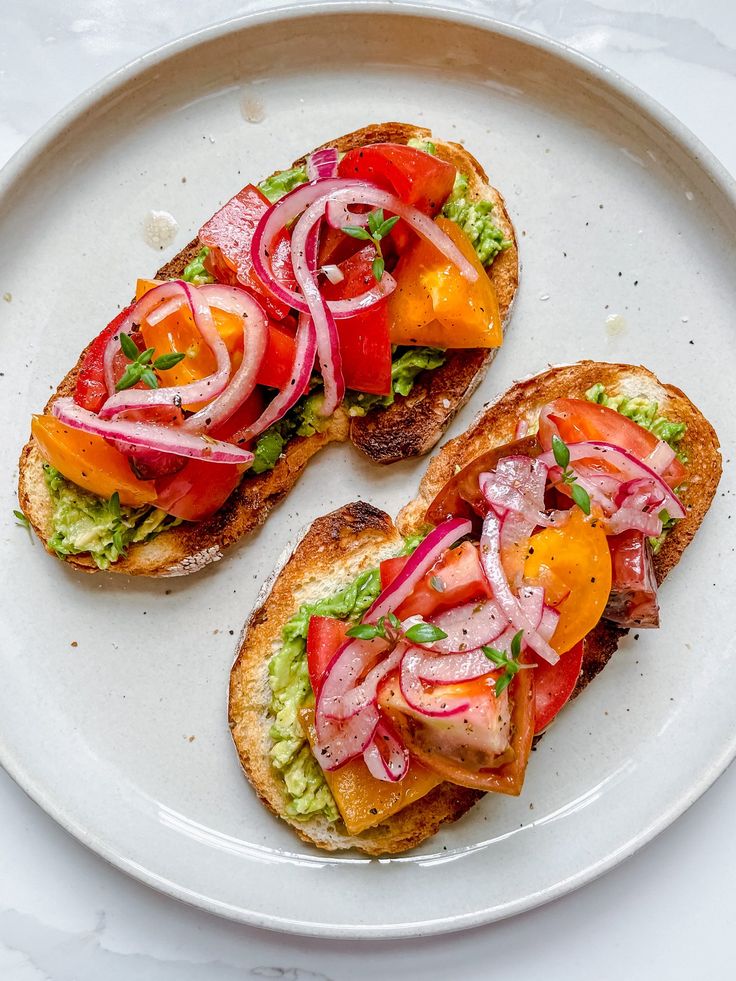 two pieces of bread with tomatoes, onions and lettuce on them sitting on a white plate