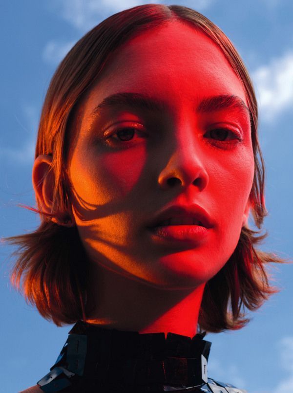 a woman with red light on her face and neck is looking at the camera while standing in front of a blue sky