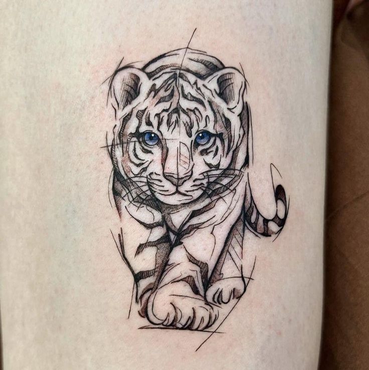 a tiger tattoo on the thigh with blue eyes and an arrow in it's mouth