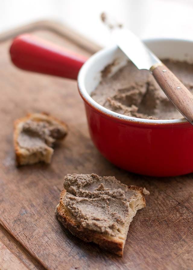 a red bowl filled with peanut butter next to two pieces of bread on a cutting board