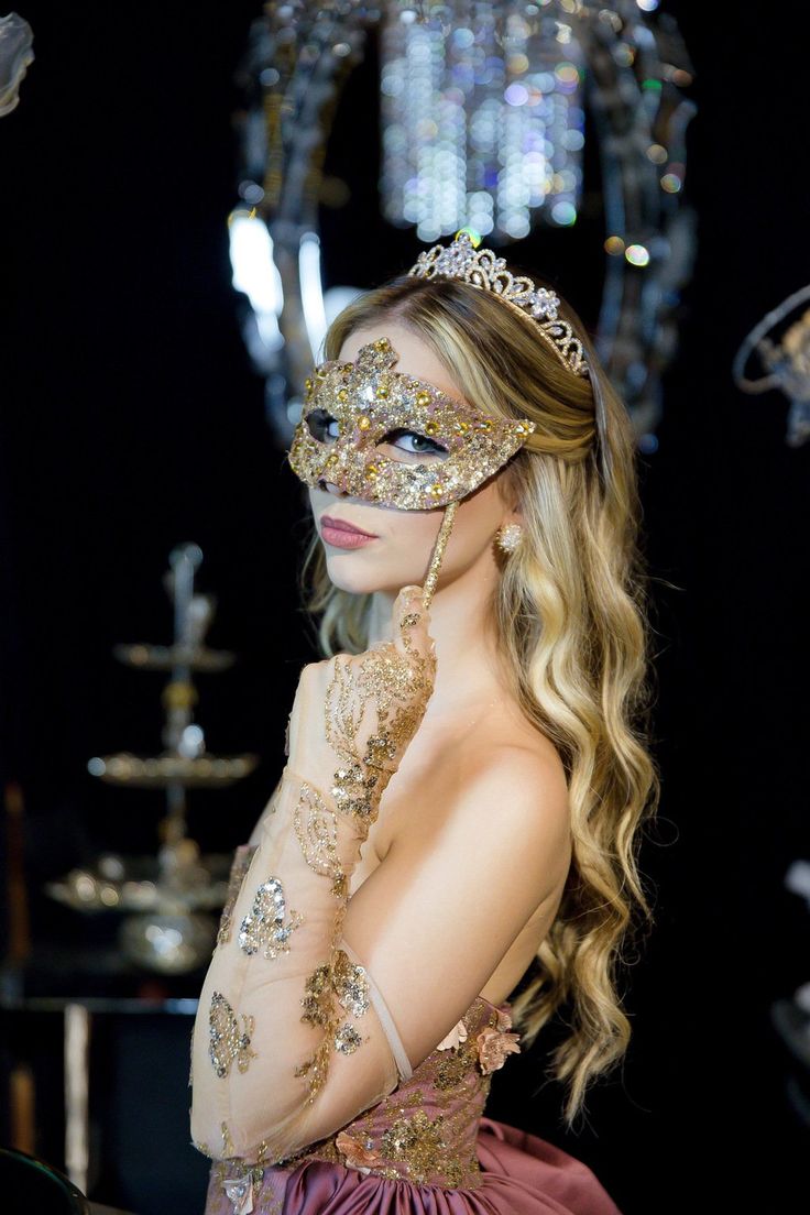 a woman wearing a mask and dress in front of a chandelier