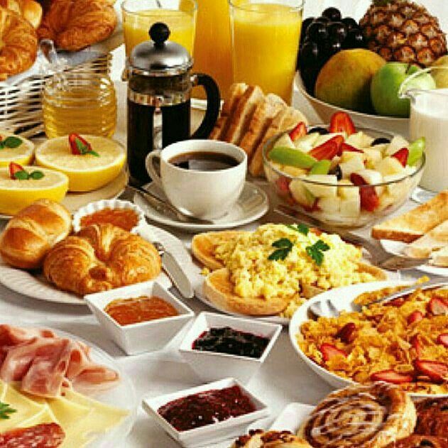 an assortment of breakfast foods and drinks on a white tablecloth with oranges, apples, croissants, coffee