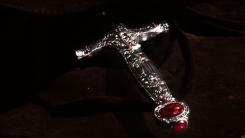 a silver cross with two red stones on it sitting on top of a black cloth