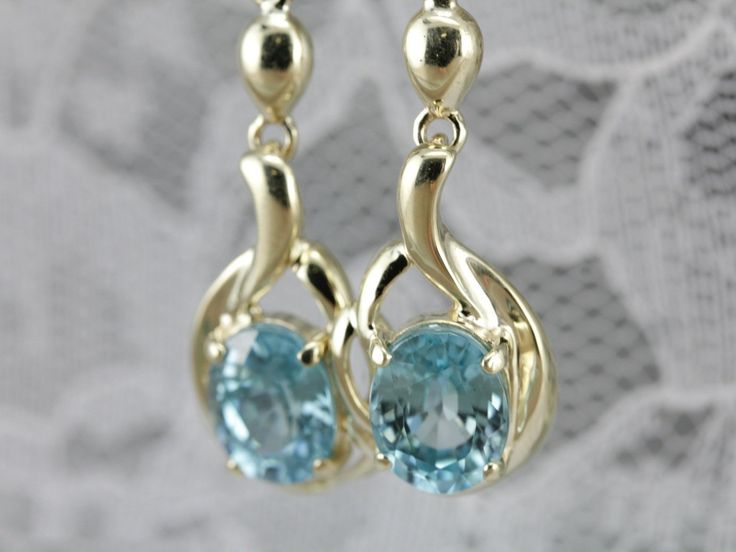 Outstanding vintage blue zircon gemstones glitter prettily from these earrings. These are teal blue stones, an unusual color that is filled with light. We've set these gems into vintage drop earrings with a pretty flourish dome that hangs perfectly just below the ear. Metal: 10K/14K Yellow Gold Gem: 2 Blue Zircon totaling 6.32 Carats Gem Measurements: 7 x 9 mm, Oval Earrings Length: 41 mm Earrings Width: 11 mm Marks: "FI 14K" Stamped on the Findings Turquoise Drop Earrings For Formal Occasions, Turquoise Earrings With Gemstone Accents For Formal Events, Fine Jewelry Topaz Earrings For Wedding, Oval Turquoise Earrings For Anniversary, Turquoise Oval Earrings For Anniversary, Oval Topaz Earrings For Formal Occasions, Fine Jewelry Aquamarine Earrings For Formal Occasions, Topaz Anniversary Earrings With Gemstone Accents, Formal Topaz Earrings For Pierced Ears