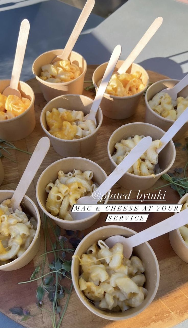 small bowls filled with macaroni and cheese sit on a wooden tray next to utensils