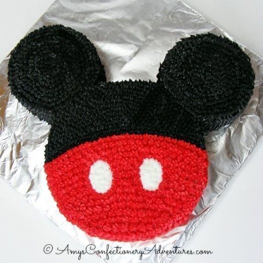 a mickey mouse cake with red and black icing on it's face, sitting on foil