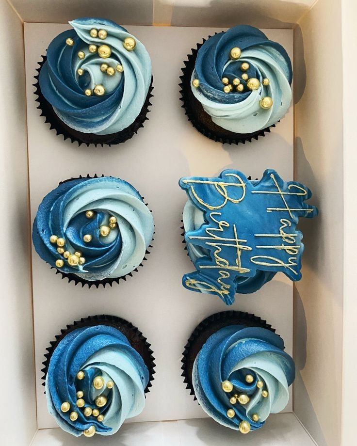 four cupcakes in a box with blue frosting and gold decorations