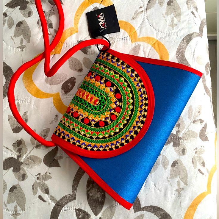 a blue and red purse sitting on top of a white bed next to a tag