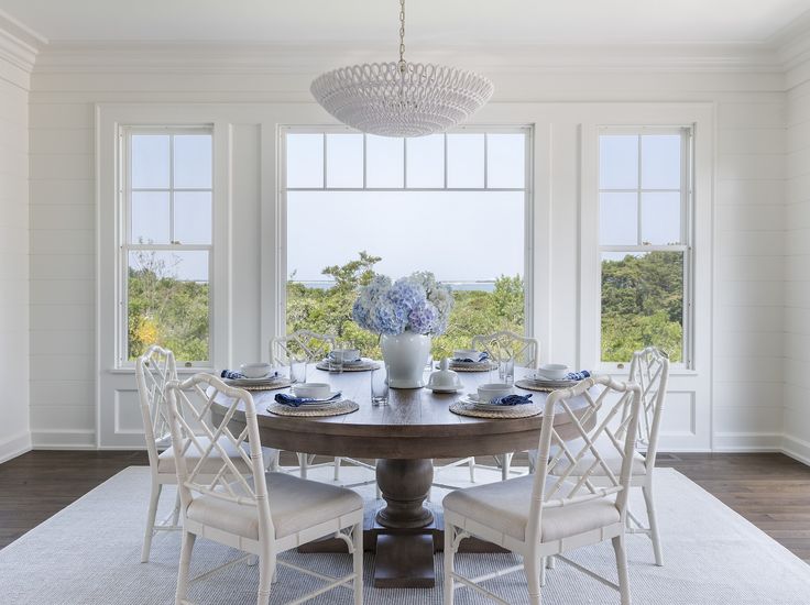 a dining room table with white chairs and blue flowers in vases on the table