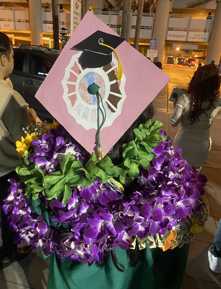 a decorated graduation cap sitting on top of a green trash can filled with purple flowers