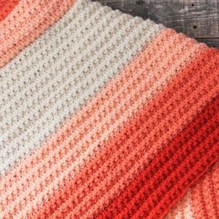 an orange and white crocheted blanket sitting on top of a wooden table