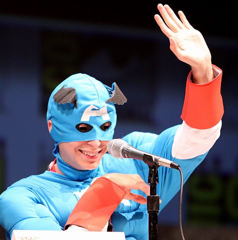 a man wearing a blue costume and mask holding a microphone in front of a microphone