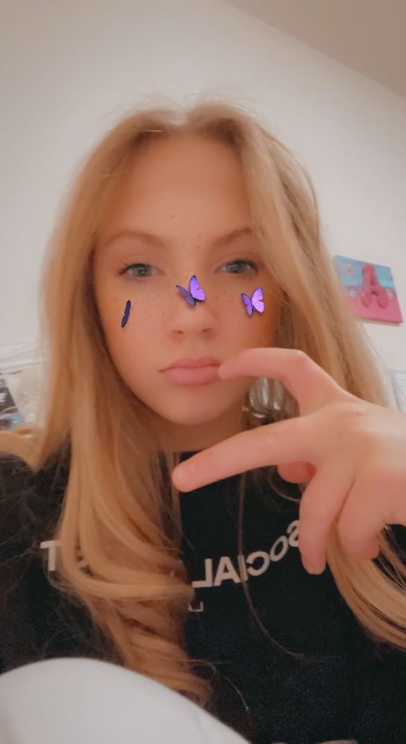 a woman with purple butterflies on her nose pointing at the camera and making a peace sign