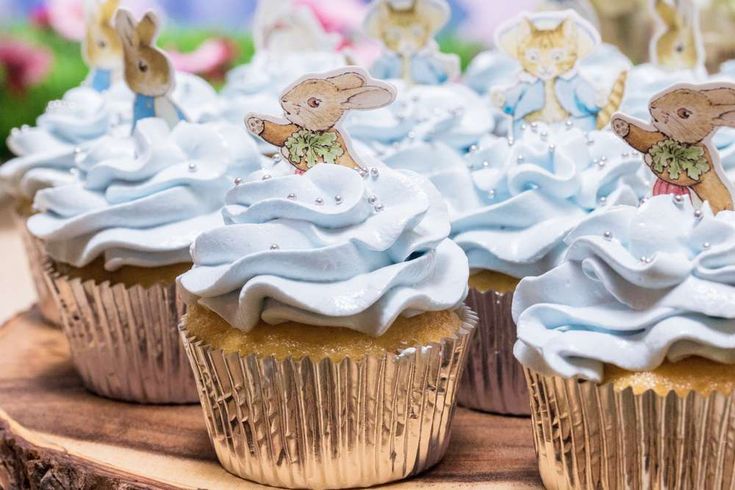 some cupcakes with white frosting and little bunnies on top are sitting on a tree stump