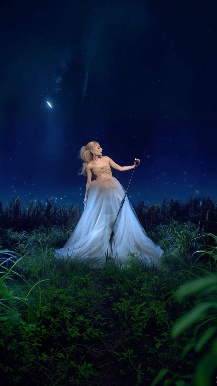 a woman in a white dress is standing in the grass at night with her arm outstretched