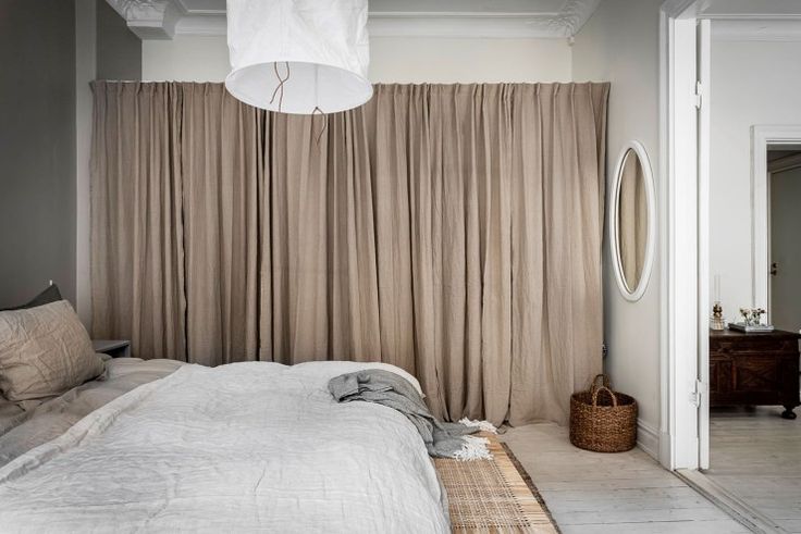 a white bed sitting under a light fixture in a bedroom next to a window with drapes