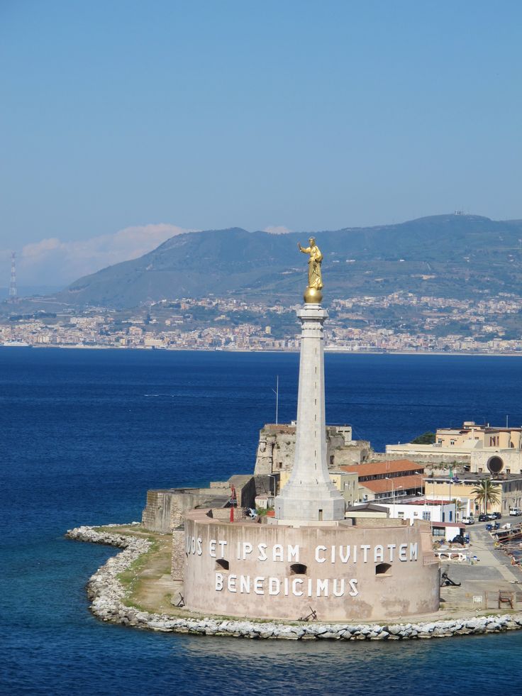 an island with a statue on it in the middle of the ocean next to a city