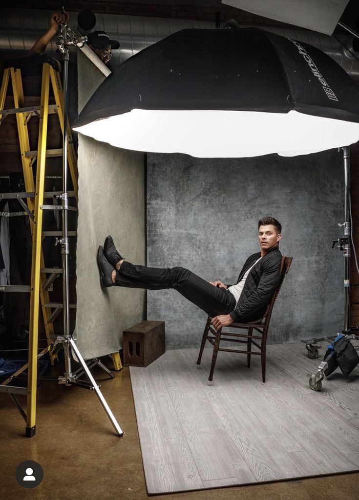 a man sitting in a chair with his feet up on the floor and an umbrella over him