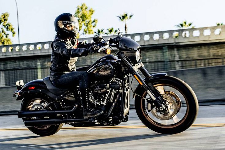 a man riding on the back of a black motorcycle down a street next to a bridge