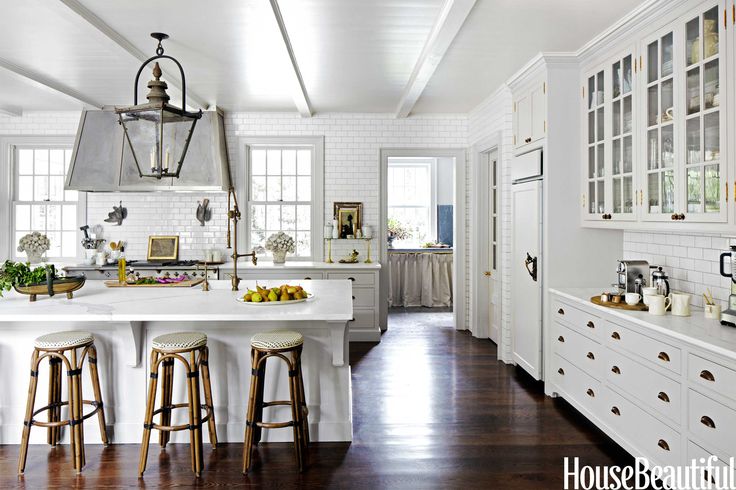 a large kitchen with white cabinets and counter tops, along with bar stools that match the hardwood flooring