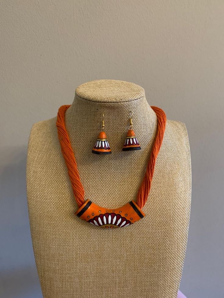 an orange necklace and matching earrings is displayed on a mannequin headdress