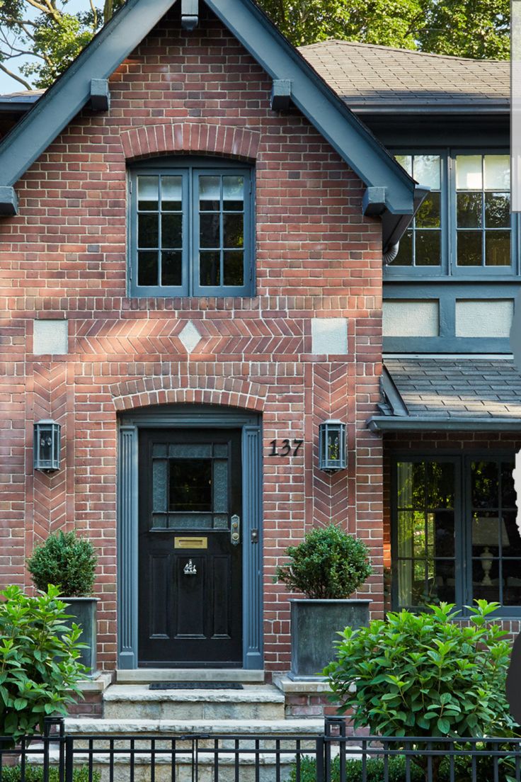 a brick house with black front door and green plants on the lawn in front of it