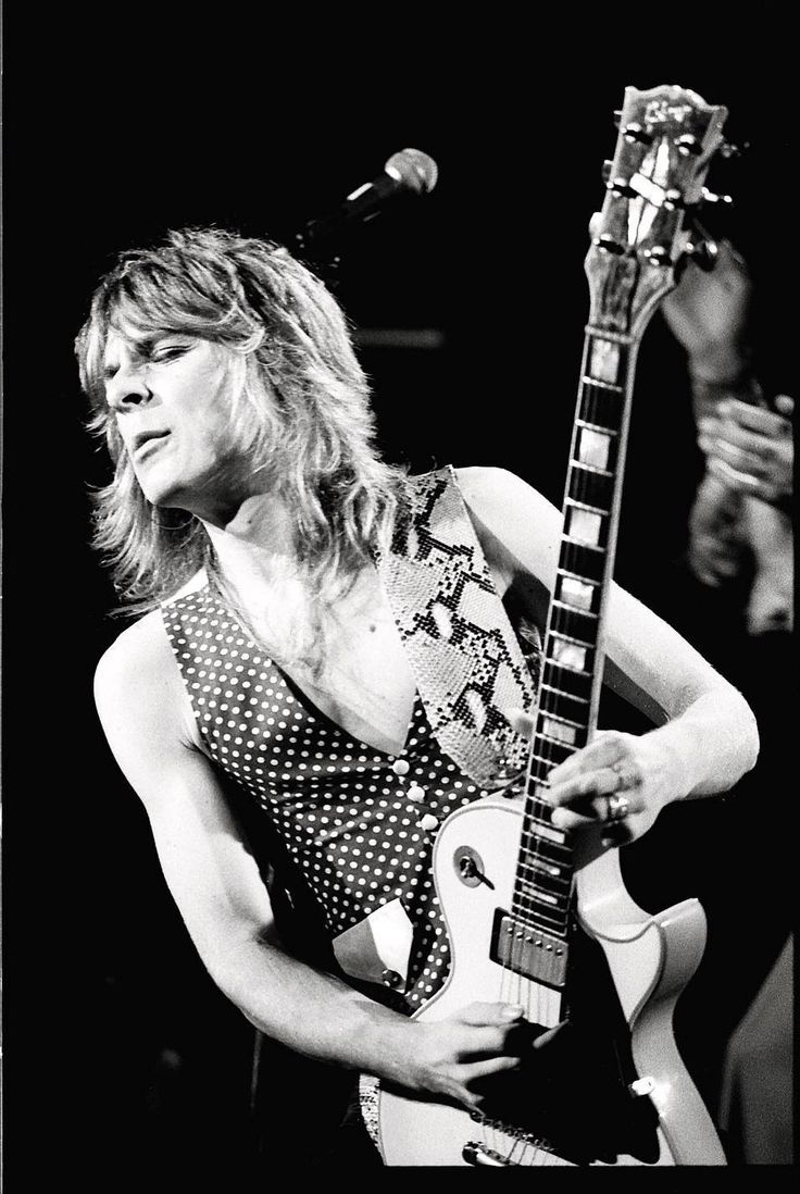 a black and white photo of a woman playing an electric guitar with a microphone in the background