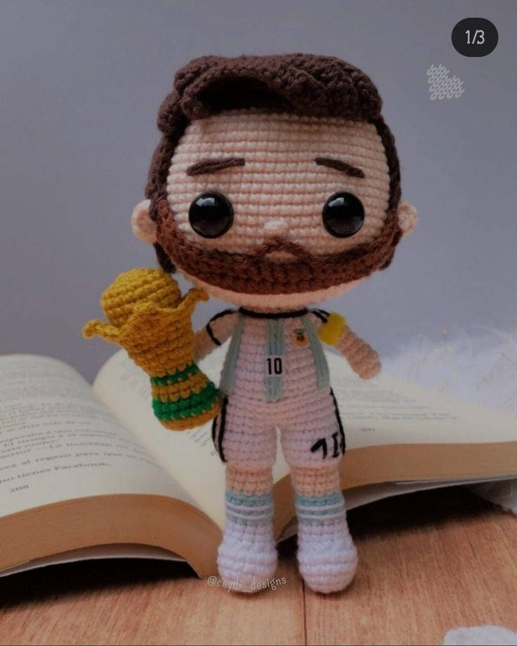 a crocheted doll is holding a book and eating something out of his hand