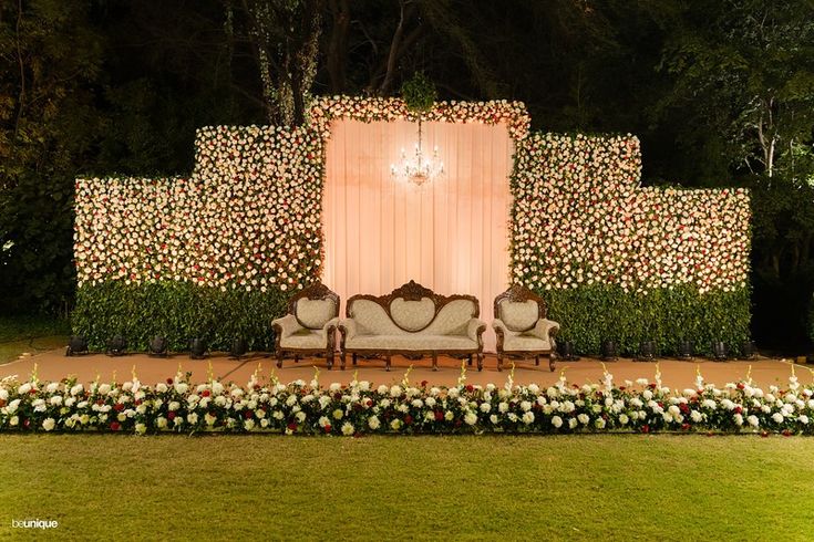 an outdoor ceremony setup with two couches and flowers on the ground, surrounded by greenery