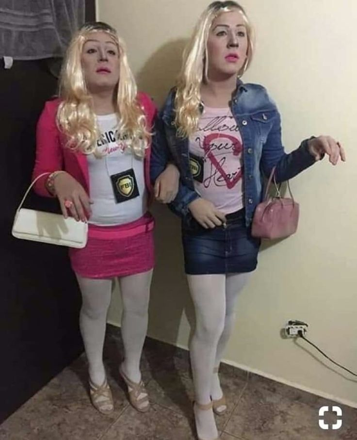 two women standing next to each other in front of a wall holding purses and cell phones