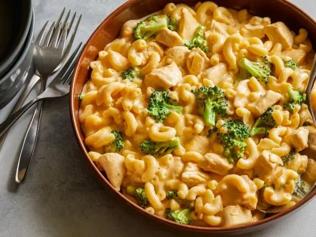 a bowl filled with macaroni and broccoli next to a fork on top of a table