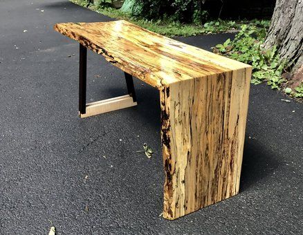 a wooden bench sitting next to a tree in the middle of a road with no leaves on it