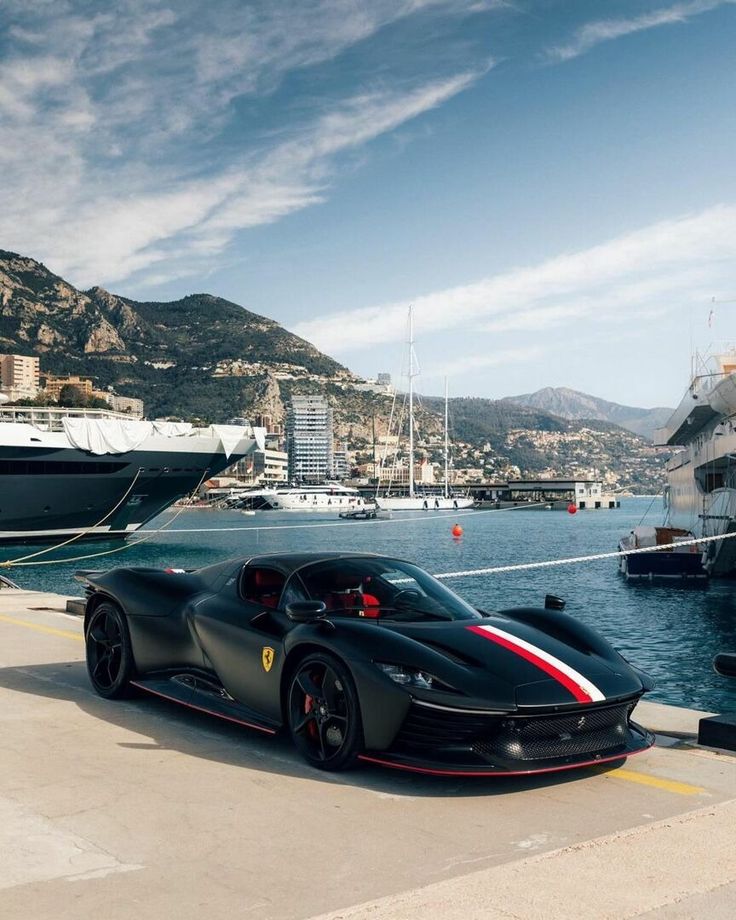 a black sports car parked next to a large boat in the water near a harbor