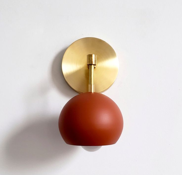 a red ball mounted to the side of a gold plated door handle on a white wall