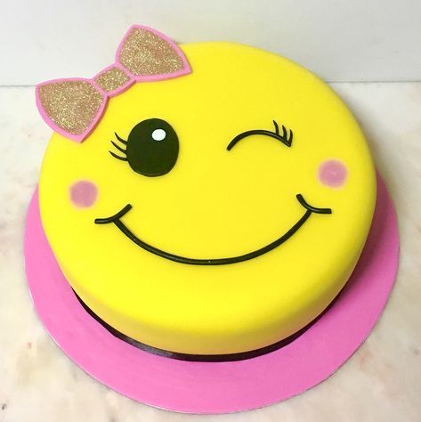 a yellow smiley face cake with a pink ribbon around its head on a white table