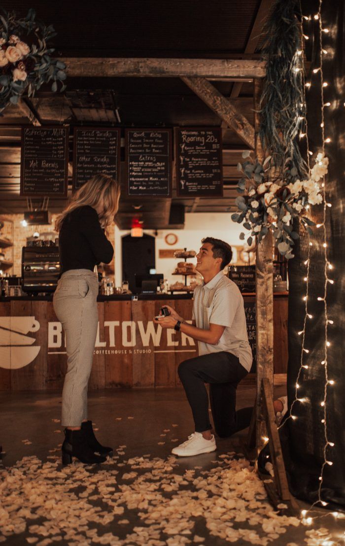 a man kneeling down next to a woman in front of a counter with flowers on it