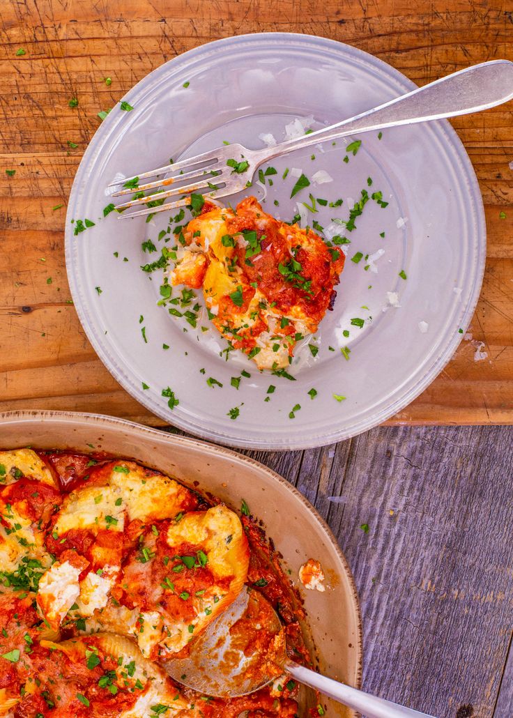 two plates with food on them sitting on a wooden table next to a fork and spoon